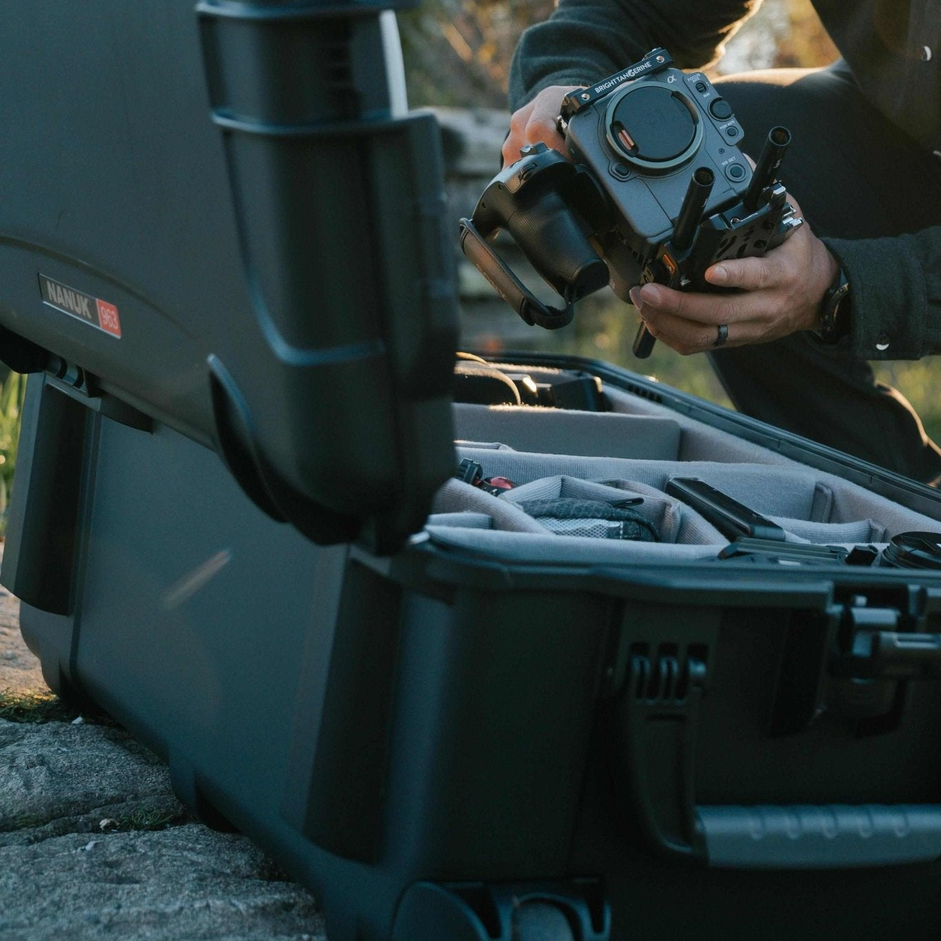 Person handling a piece of equipment near an open black case outdoors.