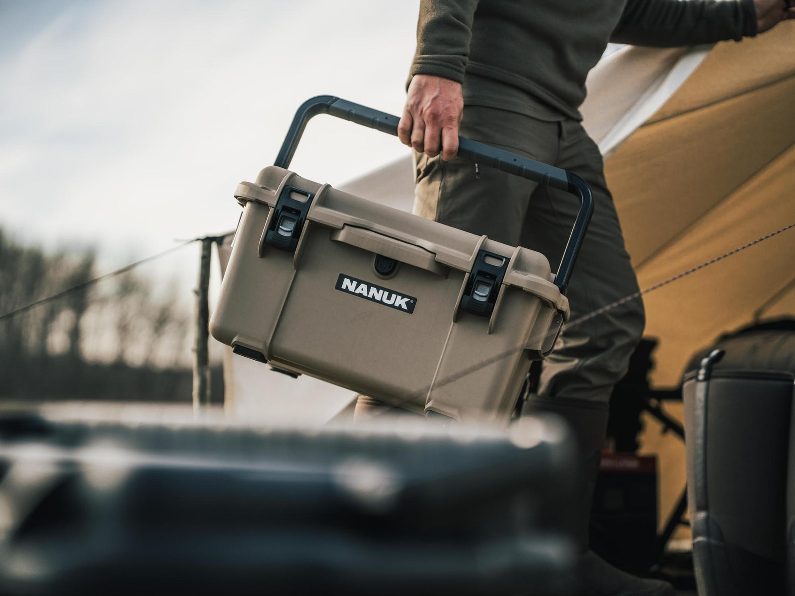 Person holding a NANUK case outdoors with a vehicle and tent in the background