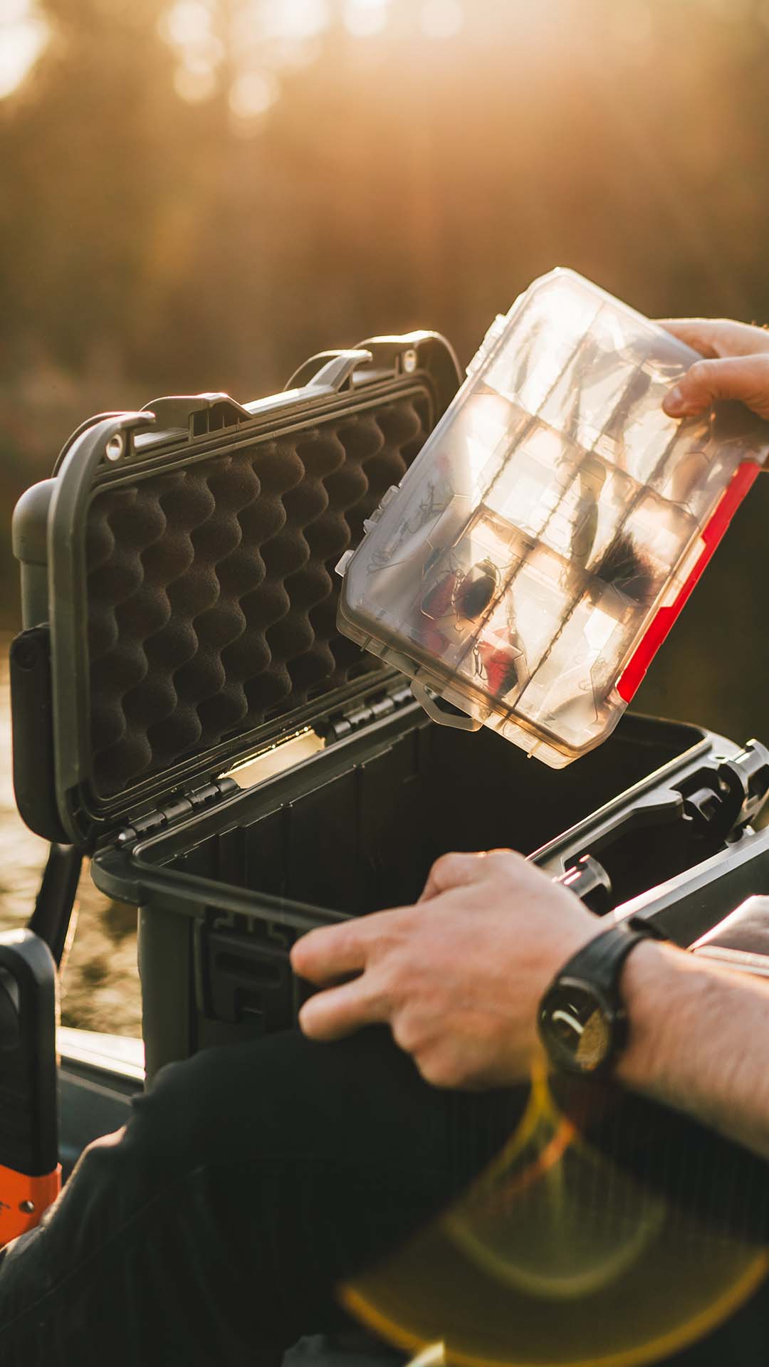 Person opening a black hard-shell case with a clear lid, holding a red and black object inside.