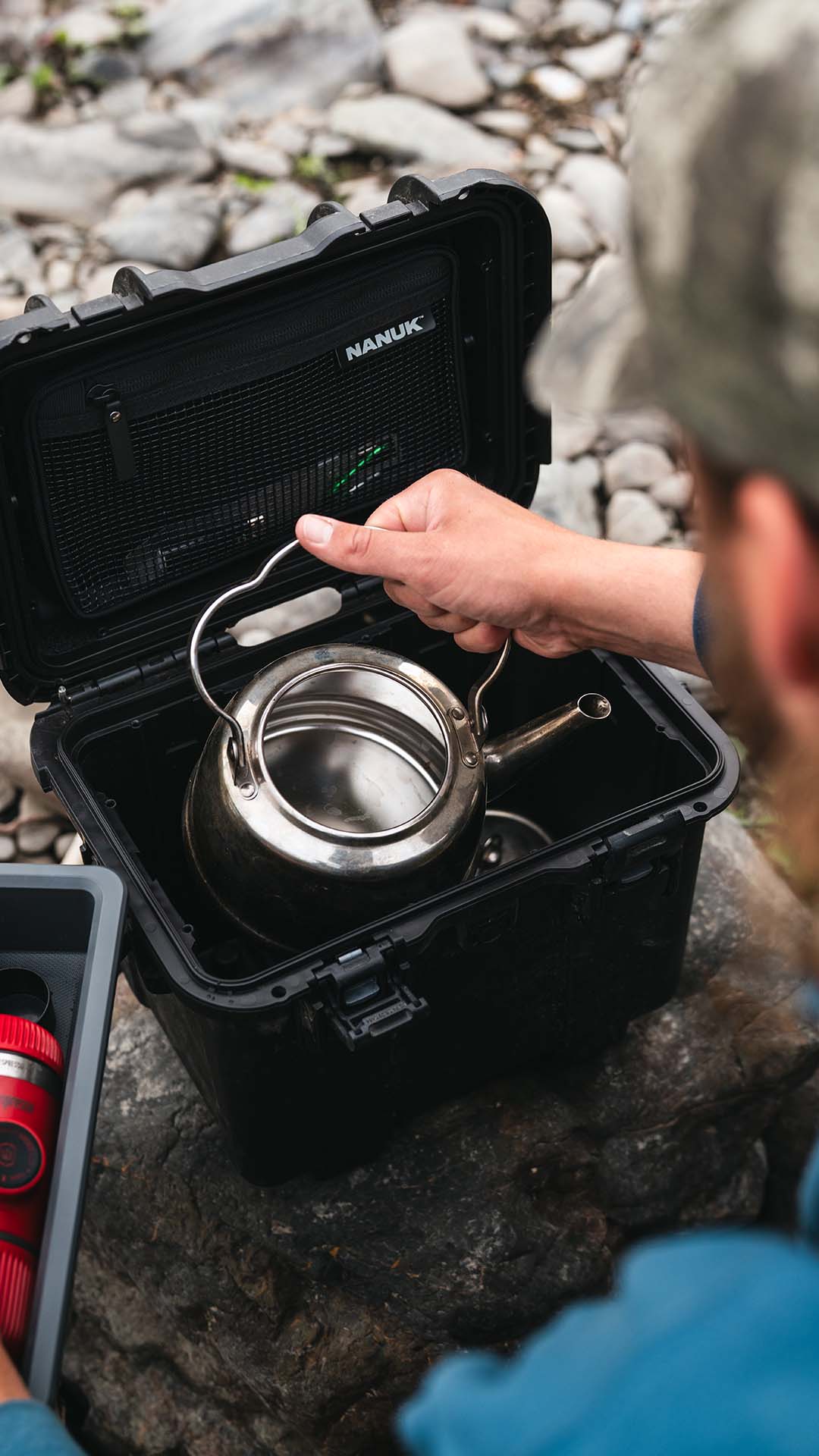 Person using a silver teapot from a NANUK case outdoors on a rocky surface