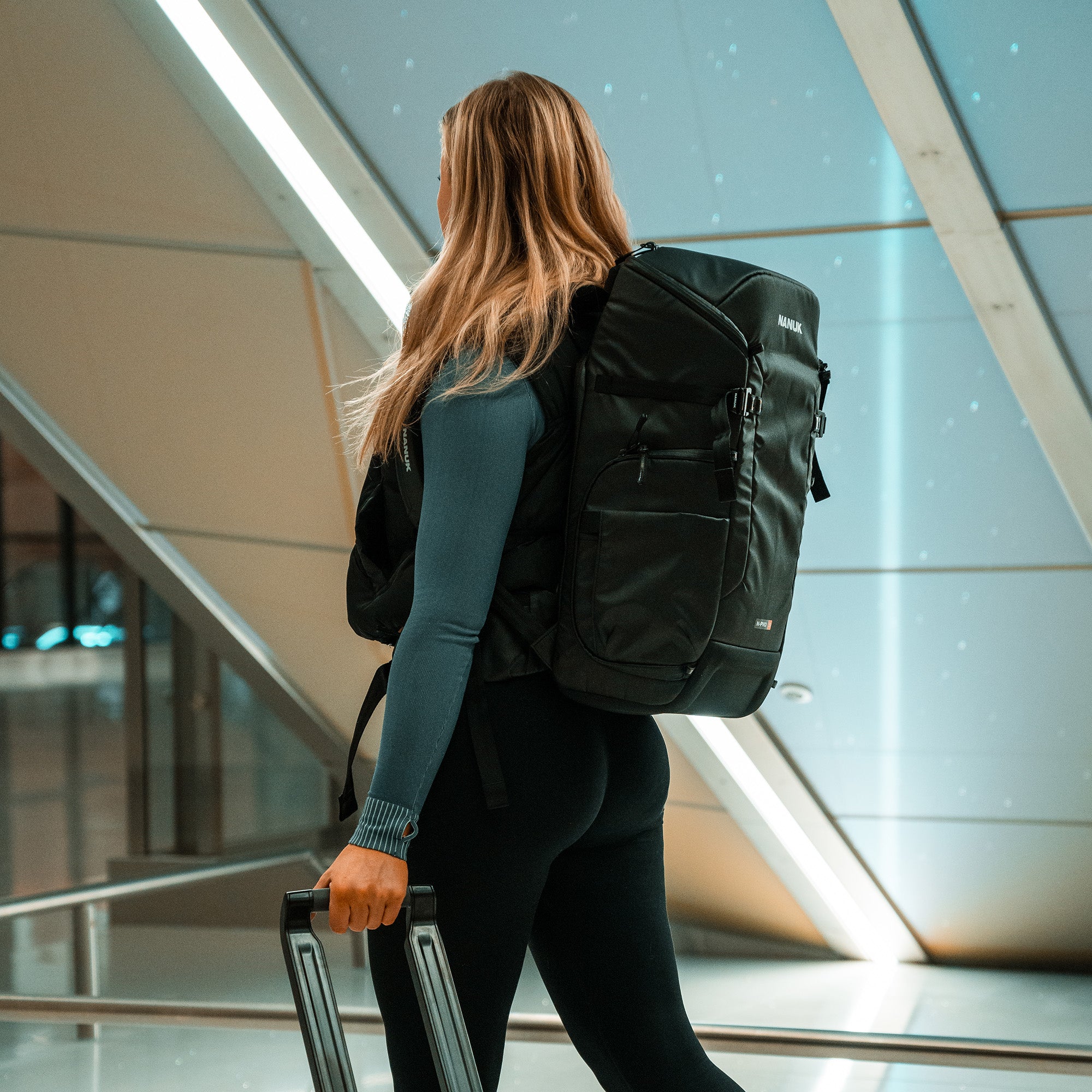 Person with a black backpack and suitcase walking through an indoor setting