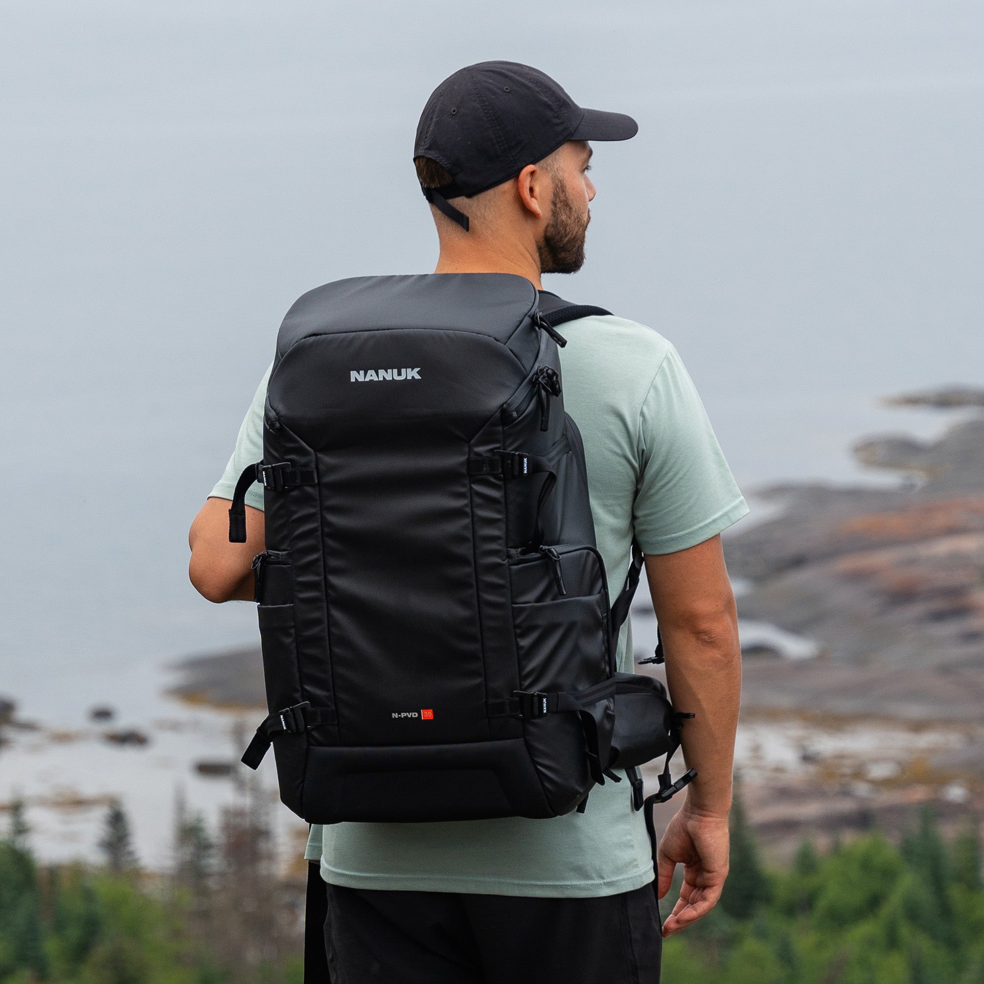 Man wearing a black Nanuk backpack with a scenic background