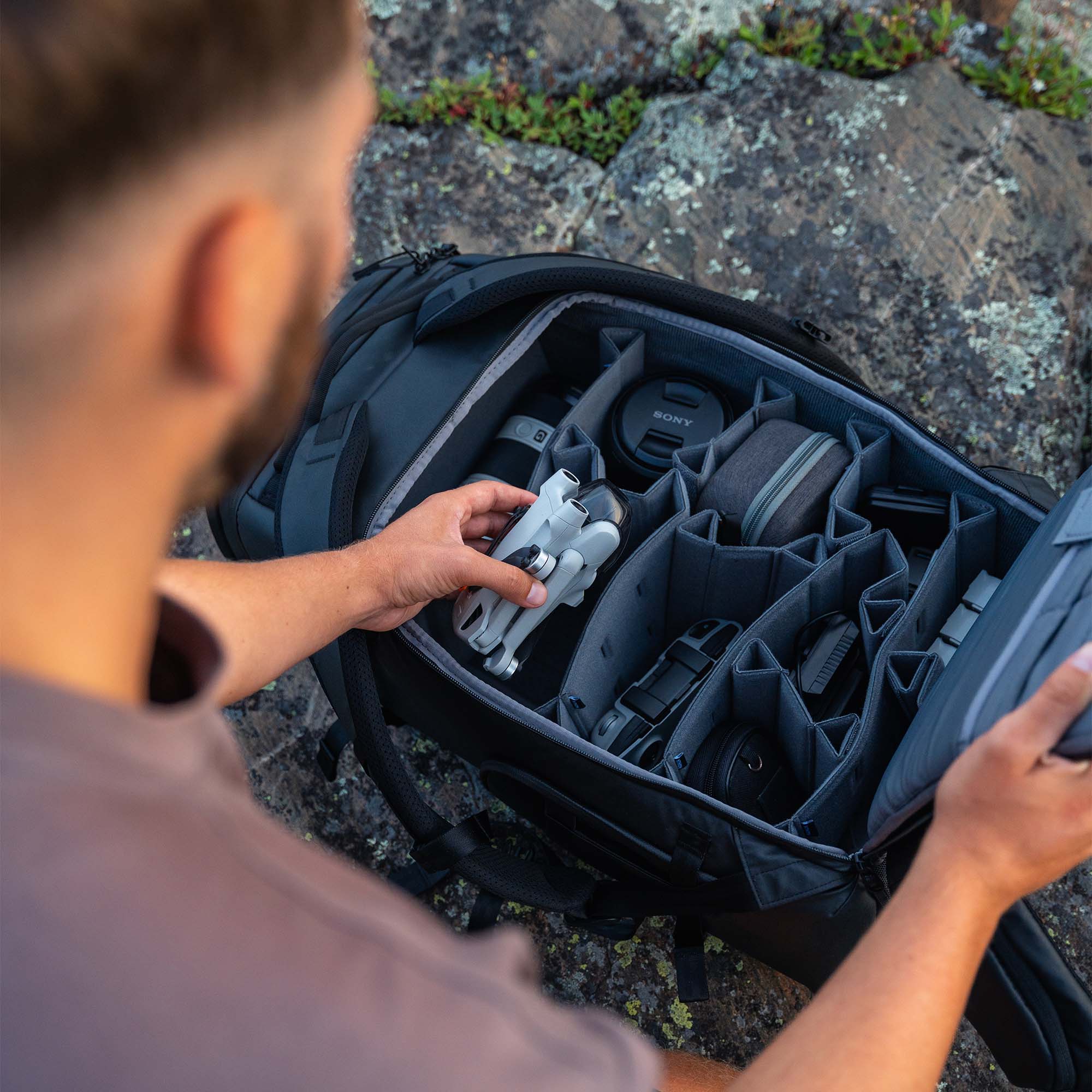 Person organizing items in a black travel bag outdoors on a rocky surface
