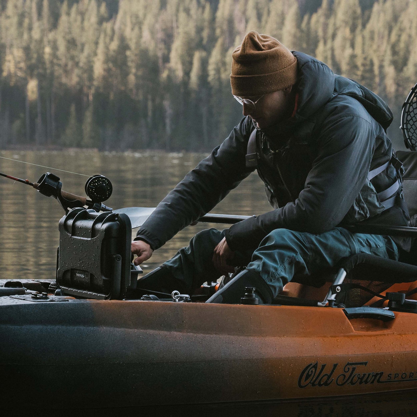 Close-up of a person fishing from a canoe, with a NANUK Trail 10 case sitting on the gunwale beside them.