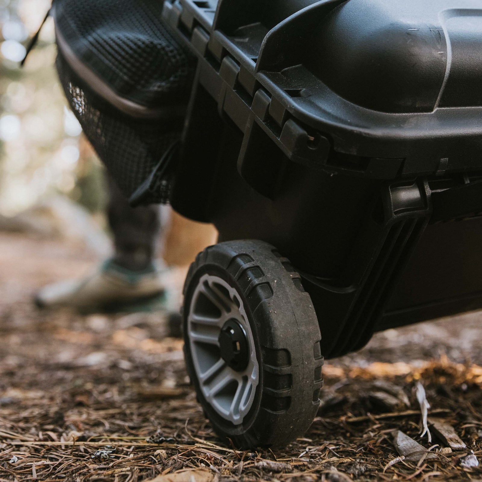 Close-up of the rugged wheel assembly on a black NANUK Trail 30 rolling case resting on a dirt path.